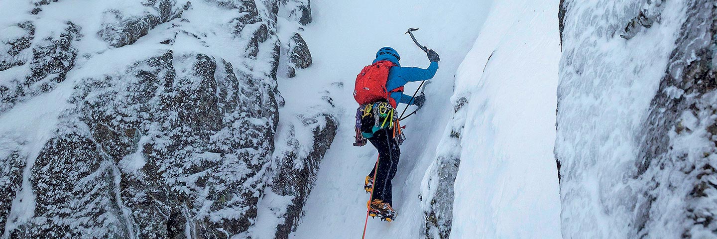 person using ice axe and crampons to climb icy gully
